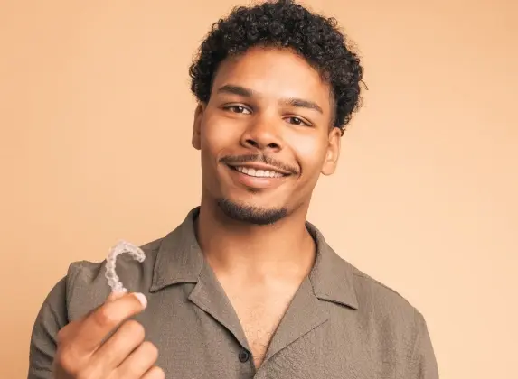 Young man smiling while holding clear aligners in Williamson, WV.