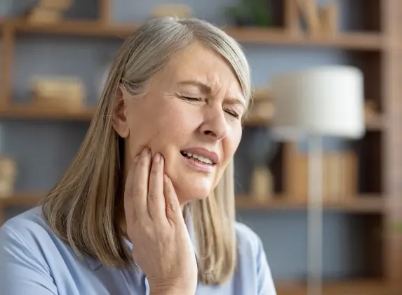 Woman experiencing tooth pain, holding her cheek while grimacing in discomfort.