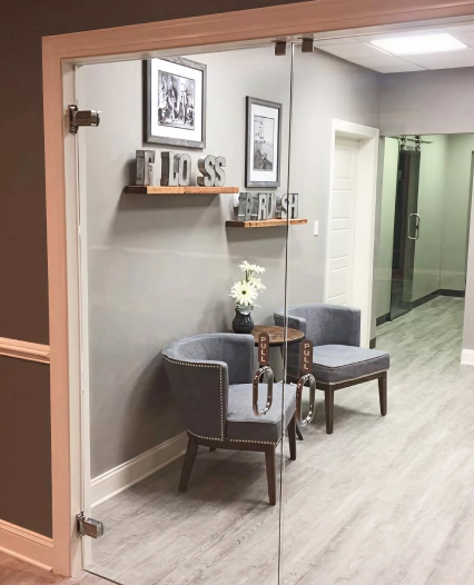 Modern dental office waiting area with seating, shelf decor, and glass entrance door.