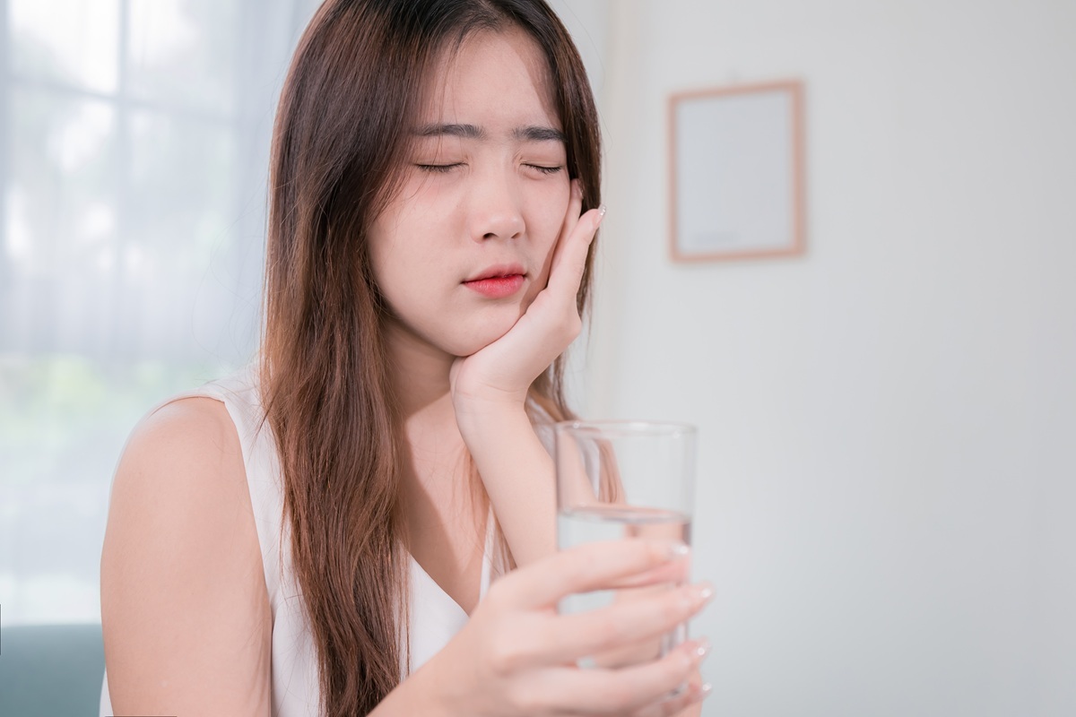 Woman holding glass of water with hand to cheek, experiencing throbbing tooth pain.