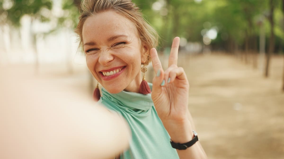 Happy woman making peace sign with beautiful natural smile outdoors.
