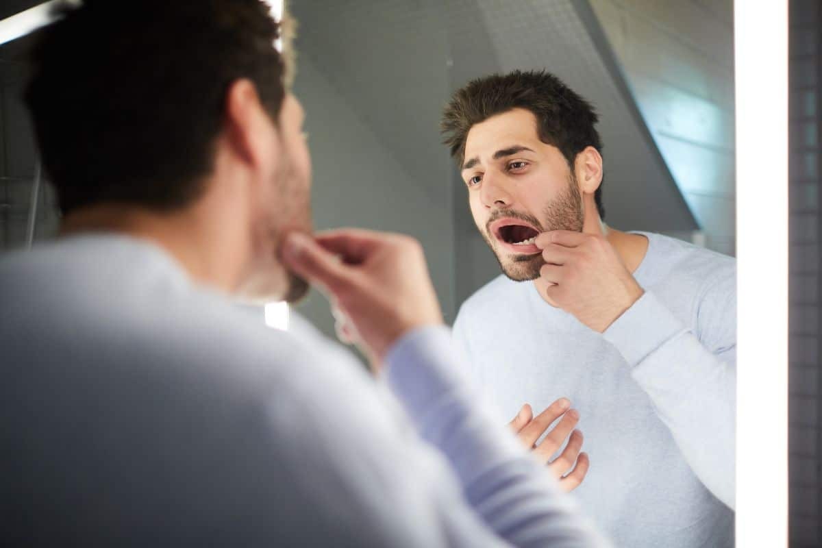 Man examining his teeth in bathroom mirror to check for white spots.